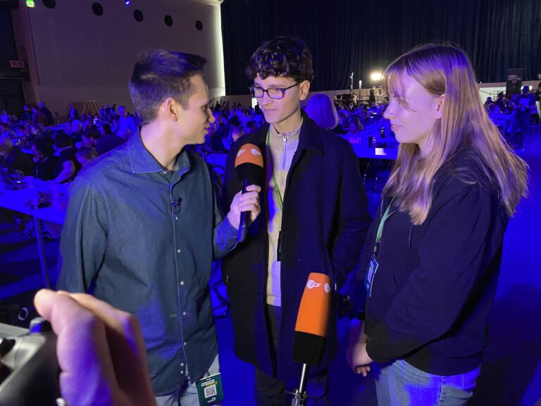 Ein Reporter mit Mikrofon vor zwei jungen Mitgliedern