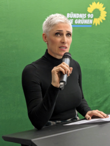 Bernadette Reinery-Hausmann vor grünem Hintergrund mit einem Mikrofon in der Hand
