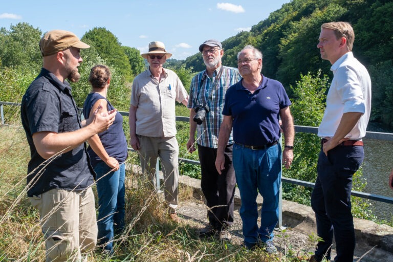 Eine Gruppe von Menschen in der Diskussion, im Hintergrund die Agger und üppiges Grün