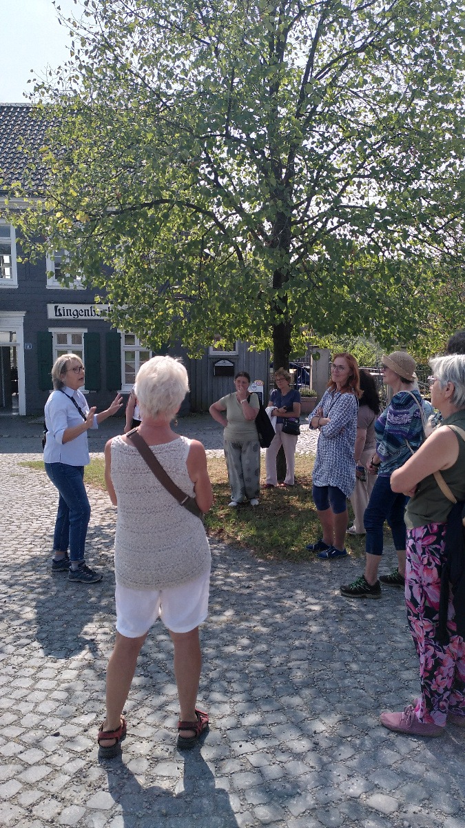 Eine Gruppe von Frauen steht unter einem Baum, im Hintergrund eine Gaststätte