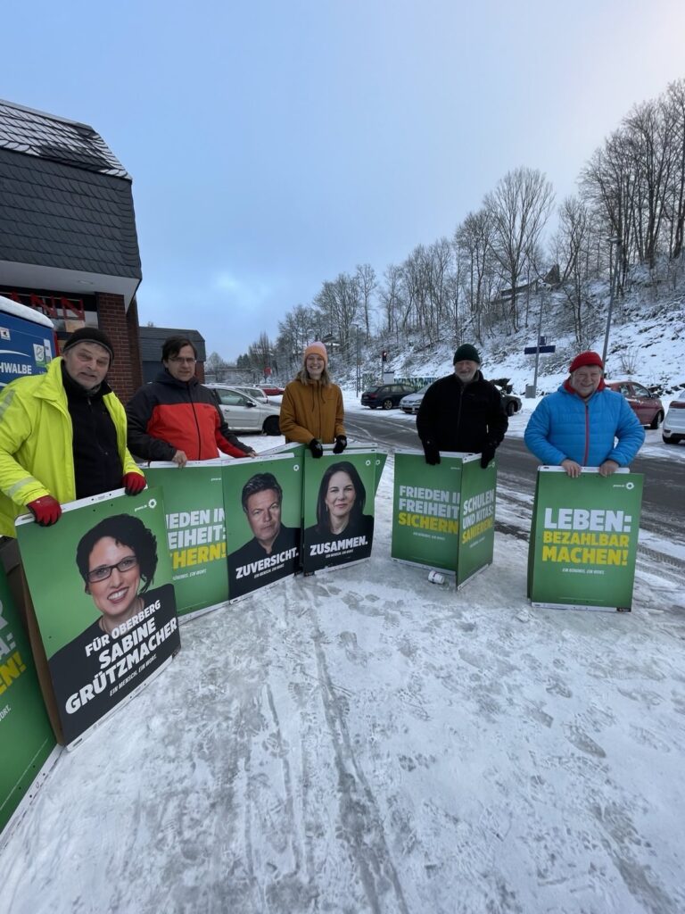 5 Personen stehn mit Wahlplakaten im Schnee