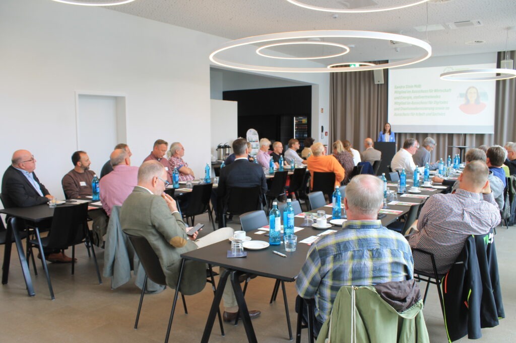 Ein heller Saal mit etwa 40 Anwesenden, die aufmerksam einer Rednerin zuhören
